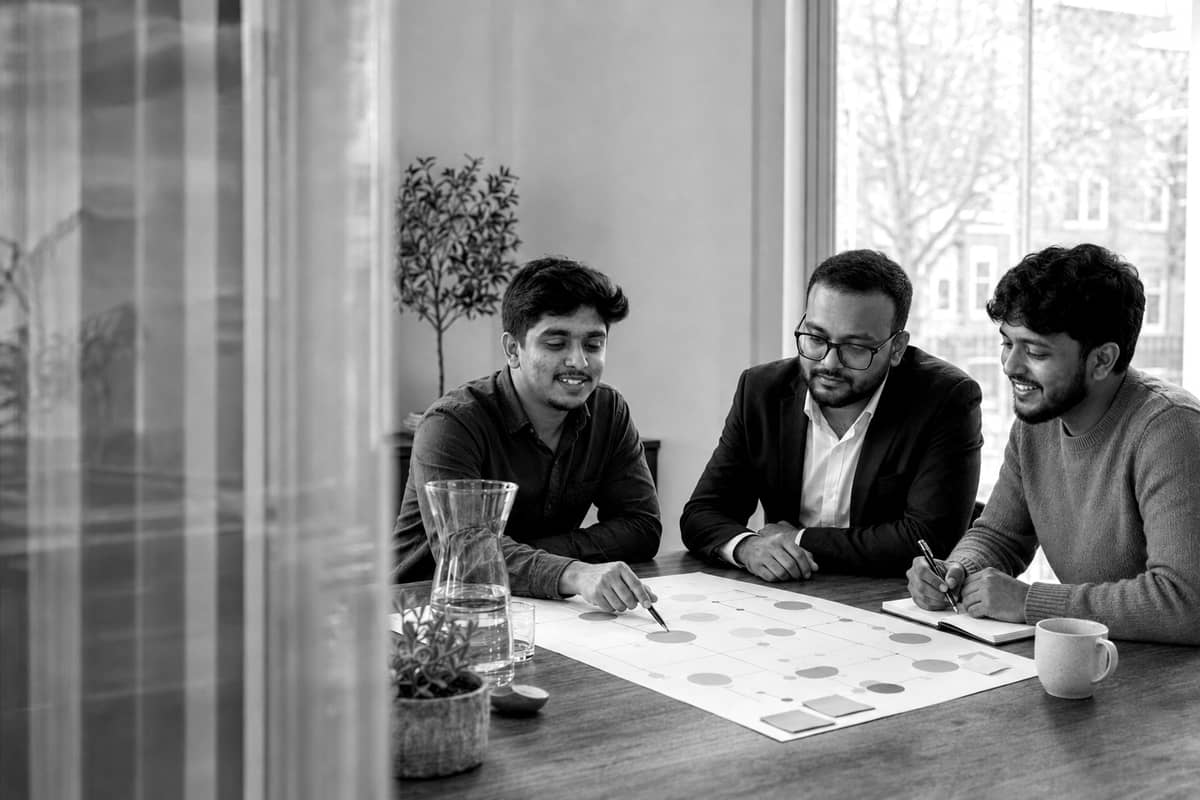 Black-and-white photo of a team in a strategy session, reviewing figures around a table